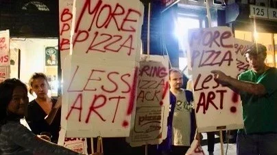 People holding signs reading More Pizza Less Art.