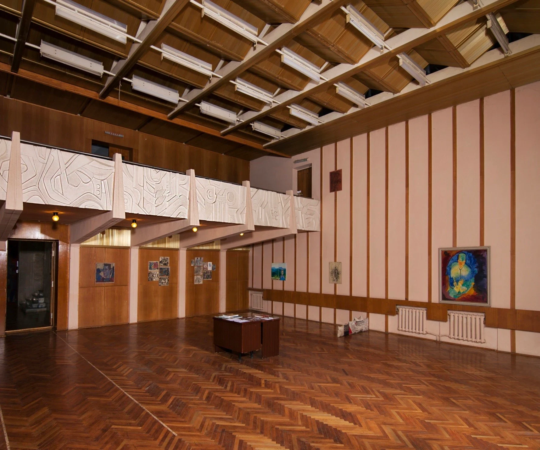 A large room with wood flooring, exposed beams and displayed artworks.