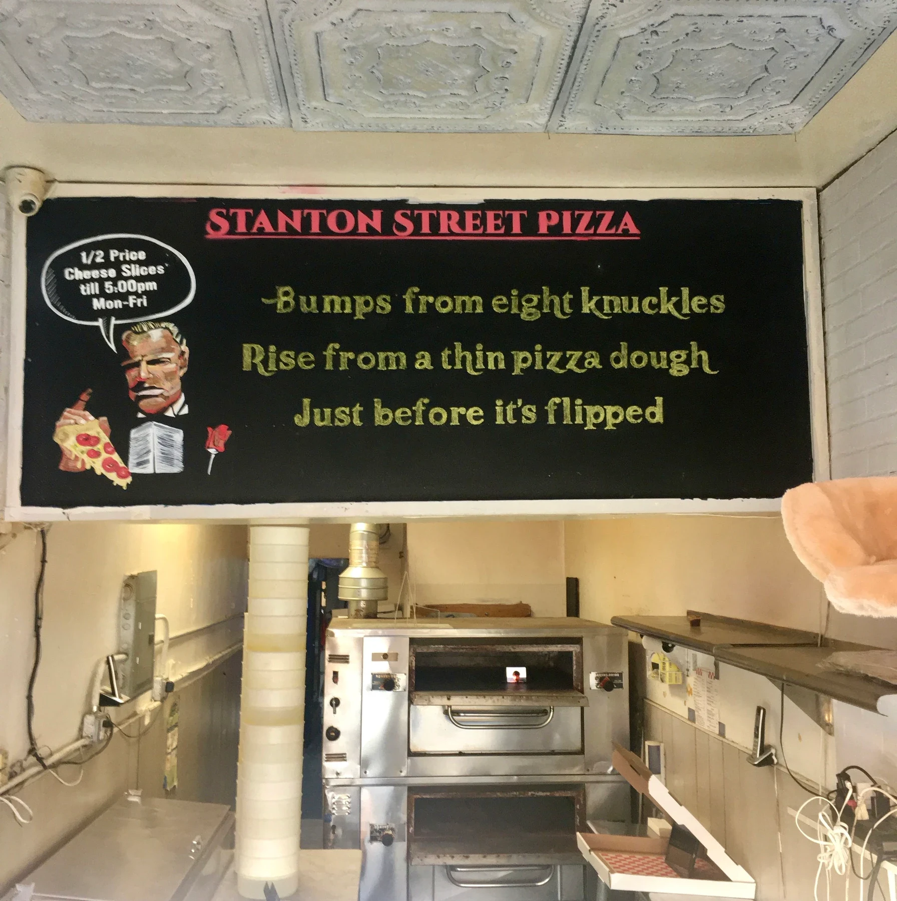 The interior of Stanton Pizza with its menu sign and metal ovens.