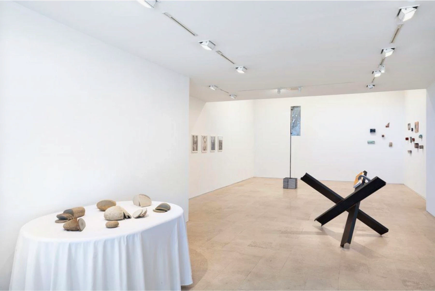 White gallery with framed works, objects on a round table and a black sculpture.