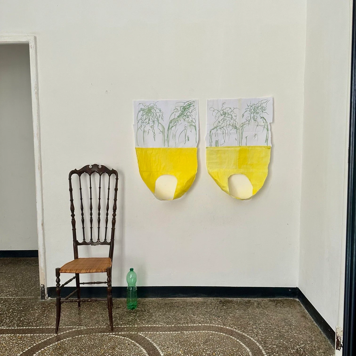 Two yellow and white paper works above a wooden chair.