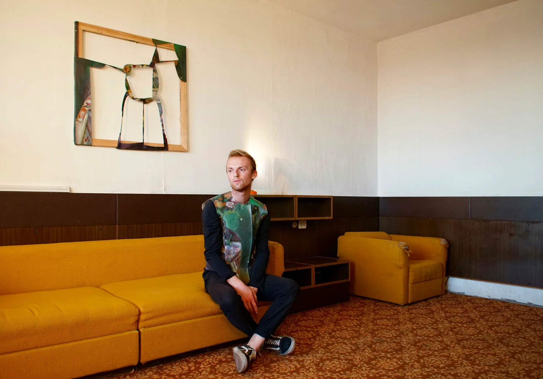A person wearing a painted garment seated on a yellow sofa.