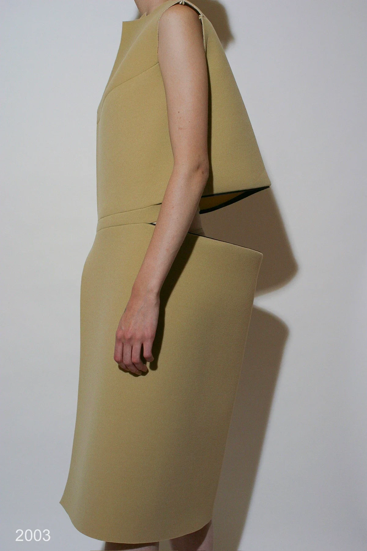 Side view of a stiff tan dress with angular projecting folds.
