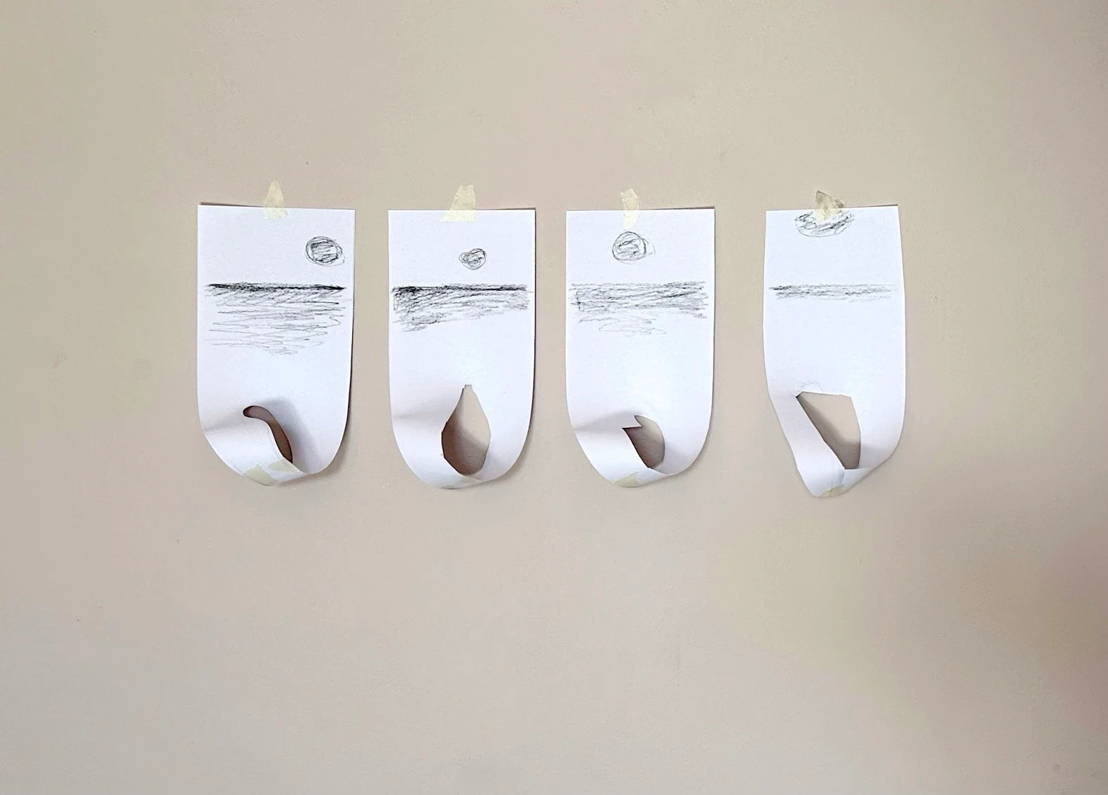 Four small paper works with curled lower edges in a row.