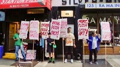 A group holding More Pizza Less Art signs outside Stanton Pizza.